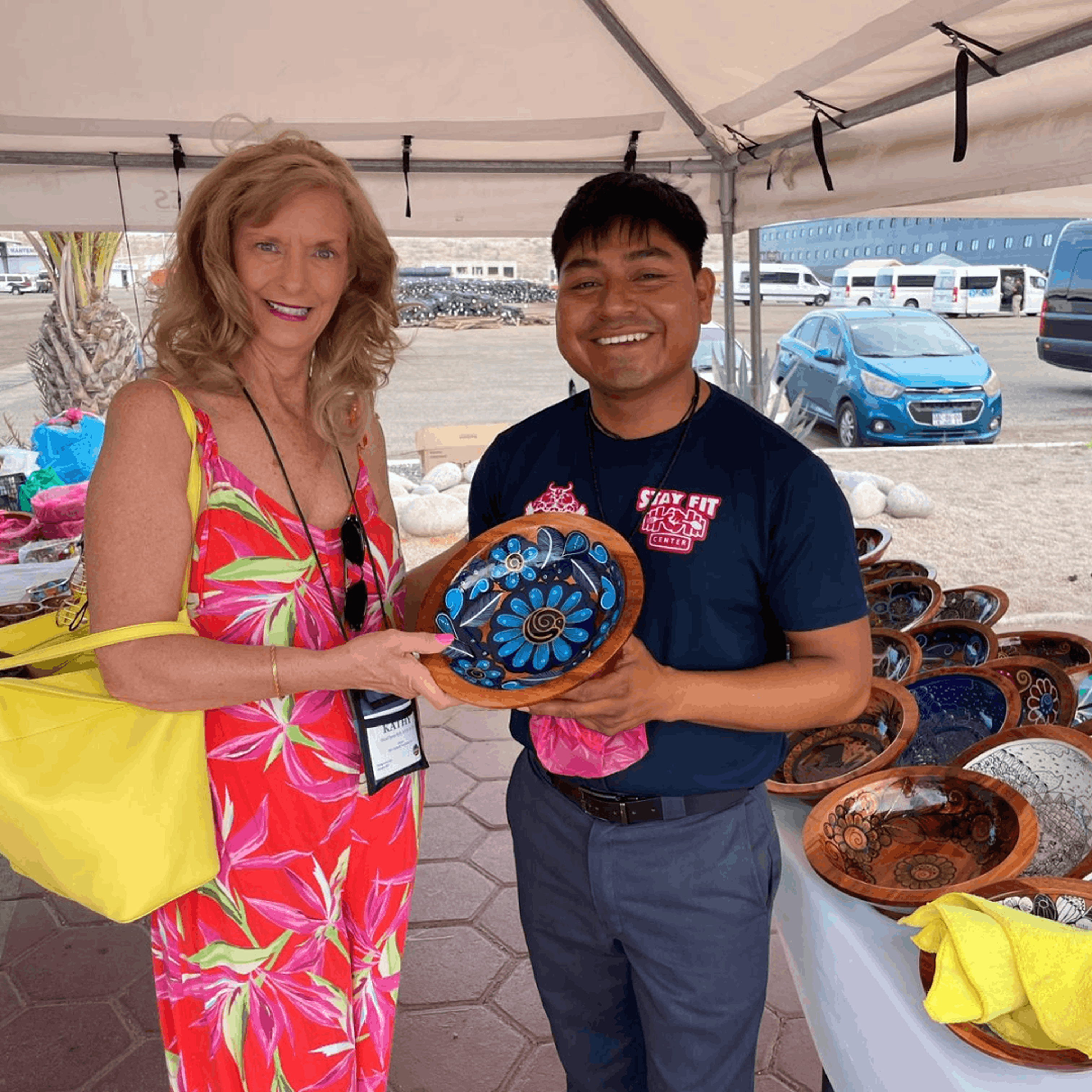 Smiling woman and artisan display a colorful hand-painted ceramic bowl at an outdoor market